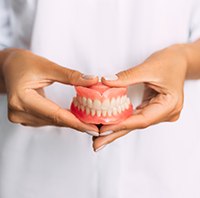 Dentist in white holding full dentures with both hands