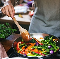 Someone in gray apron stir-frying veggies at the stove