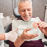 Man in red sweater in dental chair holding dentures smiling