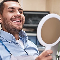 A male dental patient admiring his smile in a hand mirror