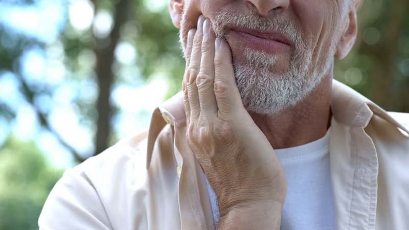 An older man rubbing his aching jaw